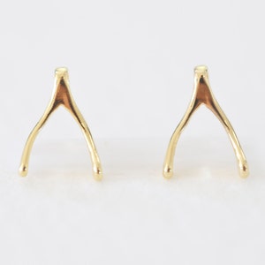 Op de afbeelding: Een paar gouden wensbeen oorbellen. De oorbellen zijn klein en delicaat en perfect voor dagelijks gebruik.