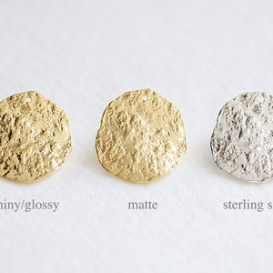 May include: Three round metal charms with a textured surface. The charm on the left is shiny gold, the middle charm is matte gold, and the charm on the right is sterling silver.