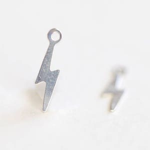 May include: A pair of silver lightning bolt earrings. The earrings are small and delicate, and they have a simple, modern design.