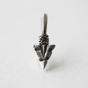 Puede incluir: Pendiente de flecha de plata con un diseño detallado. La punta de flecha es puntiaguda y tiene un bucle en la parte superior para sujetarlo a una cadena.