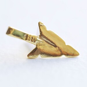 May include: A gold arrowhead charm with a pointed tip and a flat back. The charm is made of metal and has a shiny finish.