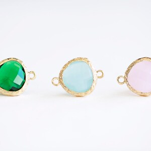 May include: Three gold-toned connector charms with different colored glass stones. The stones are green, light blue, and pink.