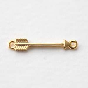 Op de afbeelding: Gouden pijlbedel met een lus aan elk uiteinde. De pijl is gedetailleerd met lijnen om op veren te lijken.