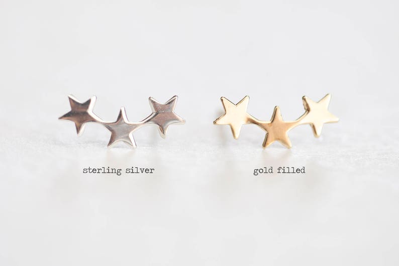 May include: Two pairs of star-shaped earrings, one pair in sterling silver and one pair in gold filled. The earrings are in the shape of three stars connected together.