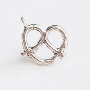 Puede incluir: Encanto de plata en forma de pretzel. El encanto es detallado y tiene un aspecto rústico.