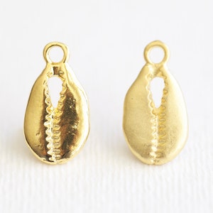 May include: Two gold-colored shell-shaped charms with a small loop at the top. The charms are detailed with a textured pattern.