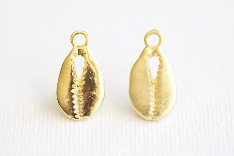 May include: Two gold-colored shell-shaped charms with a small loop at the top. The charms are detailed with a textured pattern.