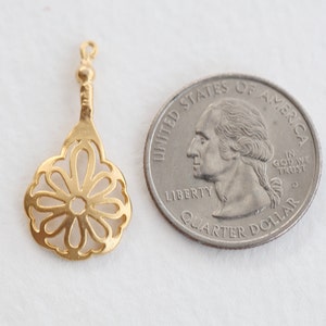 May include: A gold-colored metal pendant with a delicate, openwork flower design. The pendant is about the size of a US quarter.