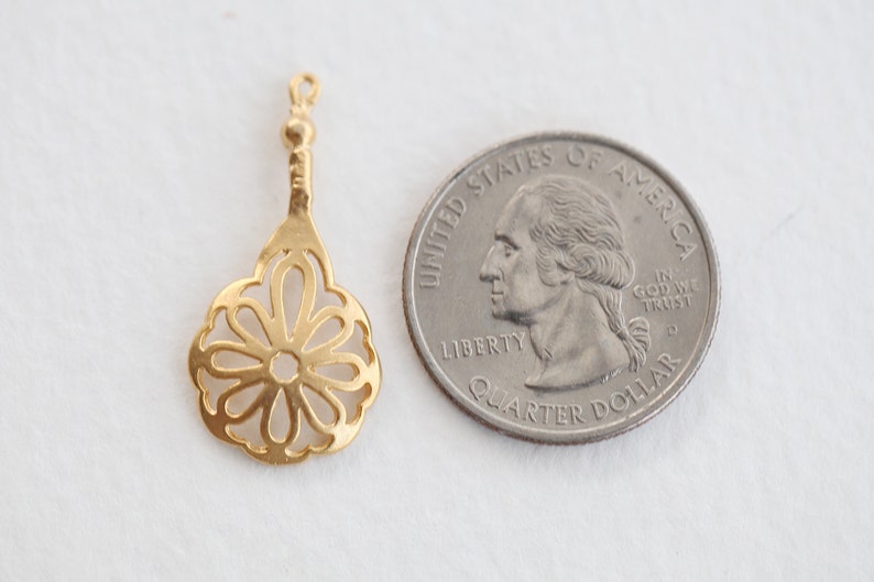May include: A gold-colored metal pendant with a delicate, openwork flower design. The pendant is about the size of a US quarter.