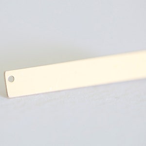 May include: A gold-colored metal bar with two small holes, one on each end. The bar is flat and rectangular.