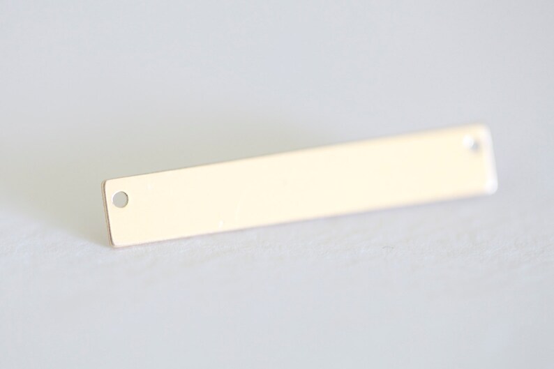 May include: A gold-colored metal bar with two small holes, one on each end. The bar is flat and rectangular.