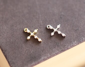 Puede incluir: Dos pequeños amuletos de cruz plateados y dorados con detalles de cristal transparente.