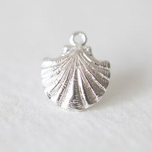 Puede incluir: Un amuleto de concha de mar de plata con una superficie texturizada detallada.