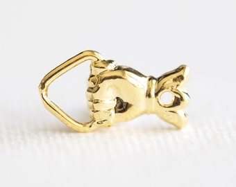 May include: Gold-toned metal clasp with a hand-shaped design and a loop for attaching to a garment. The hand is closed into a fist.
