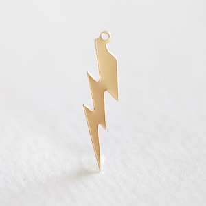 May include: A gold-colored lightning bolt charm with a small loop at the top. The charm has a jagged, zig-zag design and is likely made of metal. The lightning bolt is a popular symbol used in jewelry and accessories.