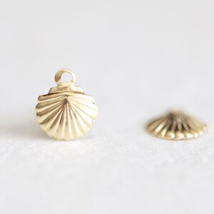 May include: Two gold-coloured metal seashell charms. One charm has a loop at the top for attaching to a necklace or bracelet. The other charm is flat and does not have a loop.