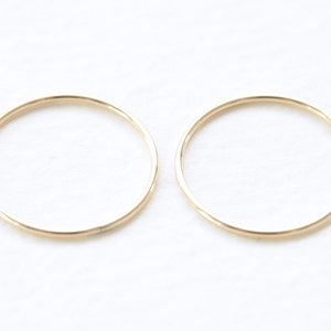 May include: A pair of thin gold hoop earrings. The hoops are simple and delicate.