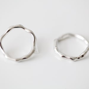 Pode incluir: Dois anéis de prata com uma forma irregular e orgânica. Os anéis são simples e modernos.