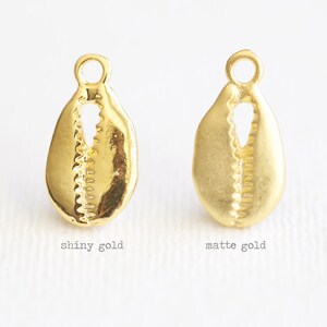 May include: Two gold cowrie shell charms, one with a shiny finish and the other with a matte finish.