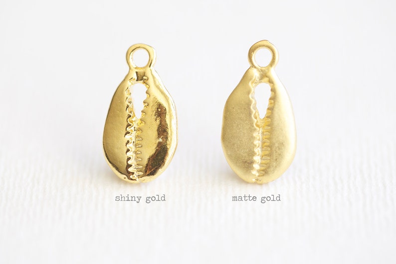May include: Two gold cowrie shell charms, one with a shiny finish and the other with a matte finish.