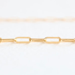 May include: A close-up of a gold chain necklace with a simple, linked design. The chain is made of small, oval-shaped links.