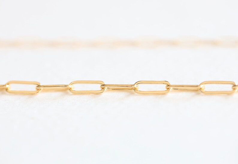 May include: A close-up of a gold chain necklace with a simple, linked design. The chain is made of small, oval-shaped links.
