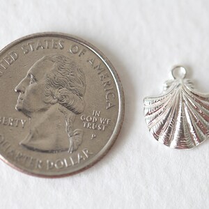 Puede incluir: Un colgante de concha de mar de plata con una superficie texturizada. El encanto es aproximadamente del tama&ntilde;o de una moneda de 25 centavos de d&oacute;lar estadounidense.