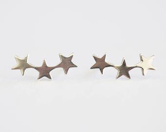 May include: A pair of silver star-shaped earrings. Each earring features five stars connected together in a curved shape.