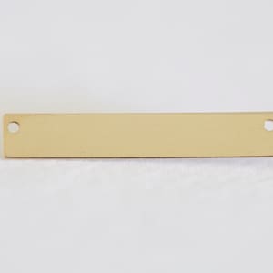 May include: A gold-colored metal bar with two round holes. The bar is smooth and has a polished finish.