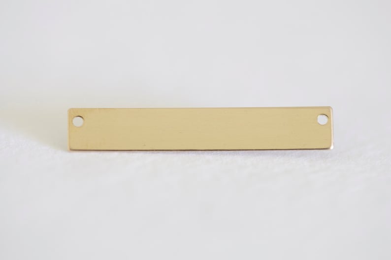 May include: A gold-colored metal bar with two round holes. The bar is smooth and has a polished finish.