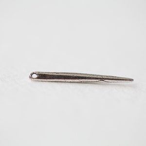 May include: A silver needle with a small eye at one end and a pointed tip at the other.