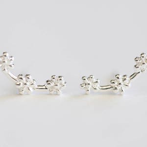 May include: A pair of silver earrings with a delicate floral design. Each earring features three small flower-shaped charms connected by a thin silver bar.