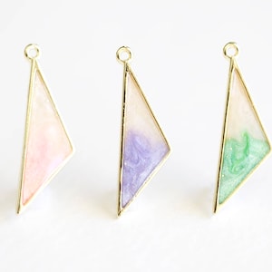 May include: Three gold triangle pendants with different colored resin inserts. The pendants are pink, purple, and green.