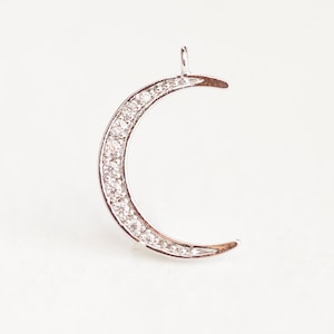 May include: A silver crescent moon charm with a row of clear cubic zirconia stones around the edge.