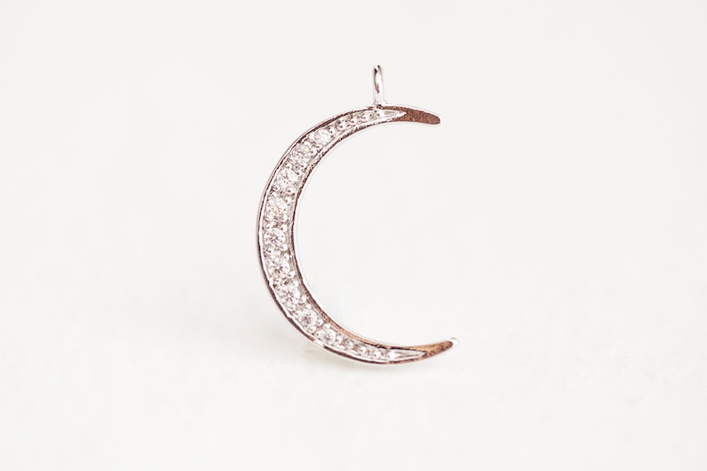 May include: A silver crescent moon charm with a row of clear cubic zirconia stones around the edge.