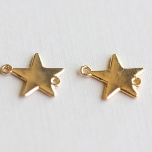 Op de afbeelding: Twee goudkleurige stervormige bedels met een lus aan elke kant. De bedels zijn perfect om een ​​toets van glans toe te voegen aan sieraden of knutselwerk.