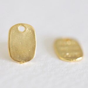 May include: Two gold-colored metal tags with a rounded oval shape and a small hole at the top. The tags are blank.