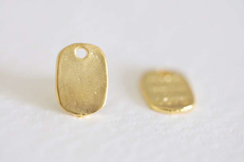 May include: Two gold-colored metal tags with a rounded oval shape and a small hole at the top. The tags are blank.
