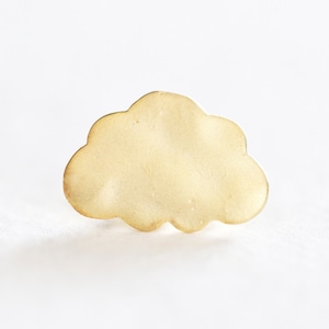 Puede incluir: Un amuleto de nube de metal de color dorado. El amuleto es liso y tiene una superficie ligeramente texturizada.
