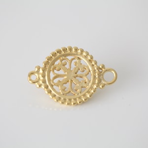 May include: Gold-toned metal connector with a decorative, openwork design in the center. The connector has two loops on either side.