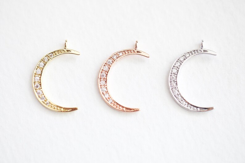 May include: Three crescent moon charms with a pave setting of clear cubic zirconia stones. The charms are available in gold, rose gold, and silver.