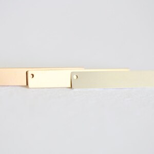 May include: Three rectangular metal tags with holes in the top. The tags are in different finishes: rose gold, gold, and silver.