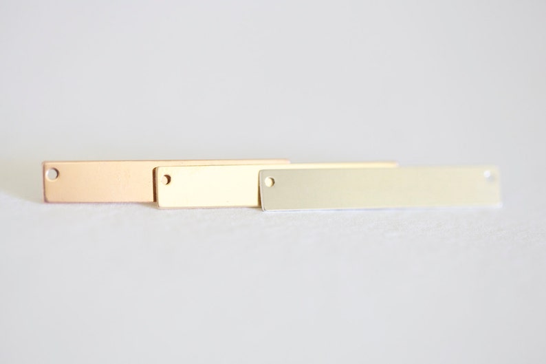 May include: Three rectangular metal tags with holes in the top. The tags are in different finishes: rose gold, gold, and silver.