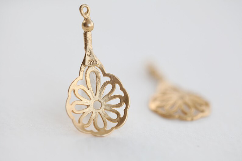 May include: A pair of gold-tone filigree earrings with a flower design. The earrings are marked "925" on the back.