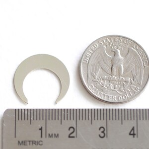 May include: A silver metal crescent moon charm, approximately 1 cm in diameter, next to a US quarter for size comparison.