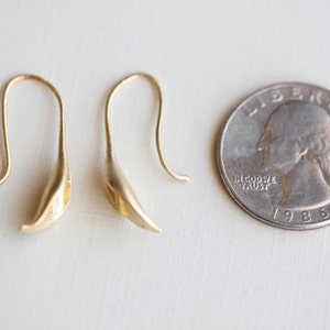 May include: A pair of gold-colored, leaf-shaped earrings with curved ear wires. A U.S. quarter coin is next to the earrings for size comparison. The coin is dated 1986.