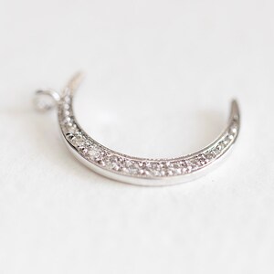 May include: A silver crescent moon charm with a row of clear sparkling stones around the edge.