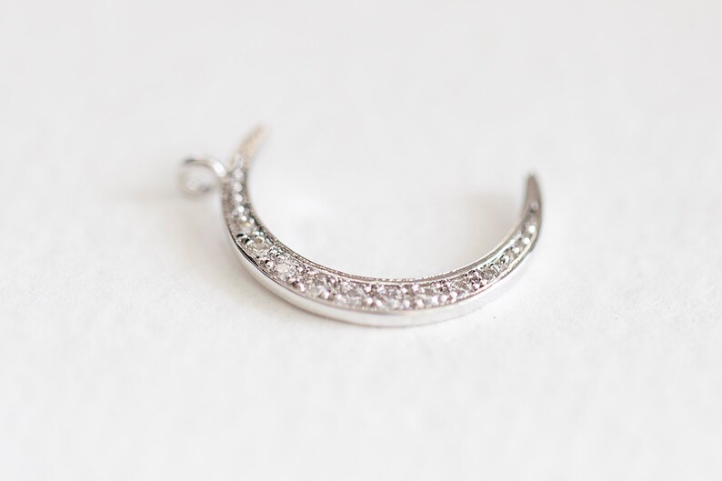 May include: A silver crescent moon charm with a row of clear sparkling stones around the edge.