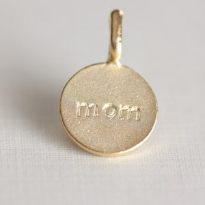 May include: Gold charm with the word "mom" engraved on it.