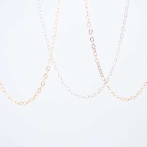 May include: Three delicate chains in gold, silver, and rose gold. The chains are made of small, oval-shaped links.